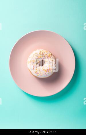 Beignet à la vanille avec saupoudrer sur une assiette rose, dessert glacé sucré sur fond bleu minimal, vue du dessus Banque D'Images