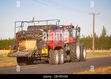 Annat, Canterbury, Nouvelle-Zélande, février 10 2020 : un tracteur agricole case rouge avec presse à foin rouge se déplace sur une route de campagne Banque D'Images