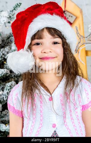 Bonne petite fille dans le chapeau du père noël devant l'arbre de noël Banque D'Images