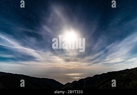 Ciel nocturne étoilé californien au-dessus de l'océan avec pleine lune derrière les nuages Banque D'Images
