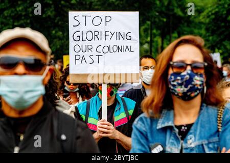 Un manifestant détient un écriteau qui dit cesser de glorifier notre passé colonial pendant la manifestation.à la suite de la mort de George Floyd alors qu'il a été détenu par la police de Minneapolis, au Minnesota, des milliers de personnes se sont rassemblées au Nelson Mandela Park à Amsterdam-Zuidoost contre le racisme. La municipalité a placé des points jaunes et blancs sur le terrain où les manifestants peuvent se tenir pour les maintenir à 1.5 mètres d'écart. Banque D'Images