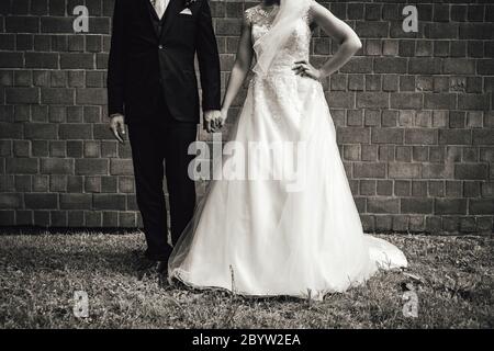 Photo noir et blanc du couple de mariage. Mariée et marié debout au mur de brique. Mariée posant avec la main sur sa hanche. Sans tête. Jour de mariage Banque D'Images