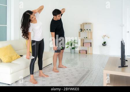 Jeune couple asiatique qui s'entraîne ensemble à l'intensité élevée et regarde la télévision à la maison, homme et femme qui s'efforcent ensemble de se tenir dans le salon, Banque D'Images