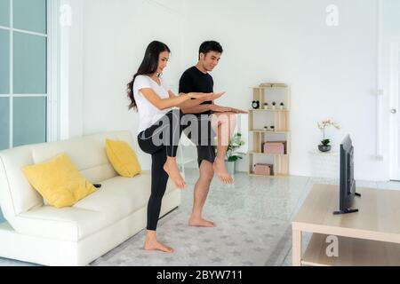 Jeune couple asiatique qui s'entraîne ensemble à l'intensité élevée et regarde la télévision à la maison, homme et femme qui s'efforcent ensemble de se tenir dans le salon, Banque D'Images