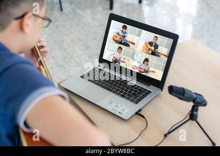 Asiatique garçon jouant de la guitare acoustique Virtual happy hour réunion pour jouer de la musique en ligne avec un ami en vidéo conférence avec ordinateur portable pour un m en ligne Banque D'Images