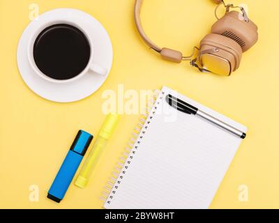 Bloc-notes photo vue du dessus Bloc-notes vide, fournitures de bureau, casque et tasse de café noir sur fond jaune Banque D'Images