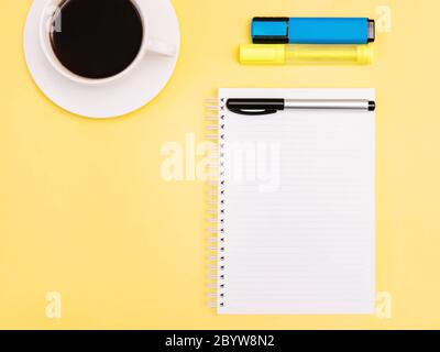 Planificateur gros plan photo en vue de dessus Bloc-notes, marqueurs colorés et tasse de café noir sur fond jaune Banque D'Images