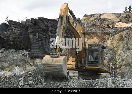 Les tapis de dynamitage en caoutchouc recyclé noir (en haut à gauche) se trouvent parmi les roches et les roches sablées, tandis qu'une pelle hydraulique de marque CAT (Caterpillar) nettoie une partie des ro sablé Banque D'Images