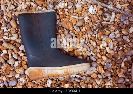 Vieille botte de gommbootte lavée sur un rivage pierreux Banque D'Images