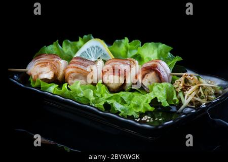 viande sur brochettes de bois, porc, poulet, poisson, pétoncle, bœuf, crevettes dans une assiette noire sur fond noir. Banque D'Images