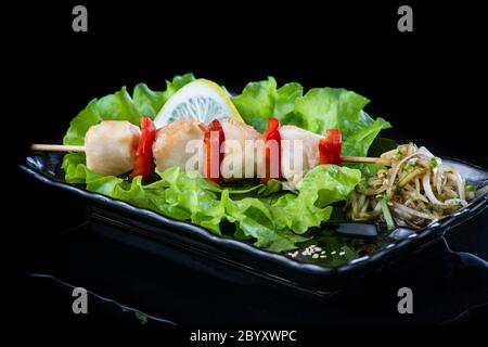 viande sur brochettes de bois, porc, poulet, poisson, pétoncle, bœuf, crevettes dans une assiette noire sur fond noir. Banque D'Images