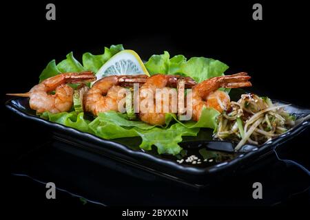 viande sur brochettes de bois, porc, poulet, poisson, pétoncle, bœuf, crevettes dans une assiette noire sur fond noir. Banque D'Images