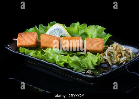 viande sur brochettes de bois, porc, poulet, poisson, pétoncle, bœuf, crevettes dans une assiette noire sur fond noir. Banque D'Images