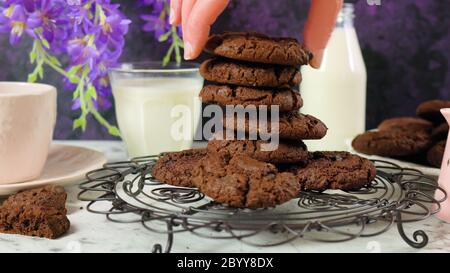 La main de femme en prend un de la pile de biscuits faits maison à double puce de chocolat dans un cadre vintage créatif sur un fond de marbre violet et blanc. Banque D'Images