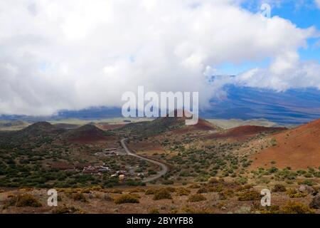 Paysage pittoresque de Mauna Kea avec route pavée jusqu'au sommet entre les vieux cratères et vue sur Mauna Loa dans les nuages. Banque D'Images