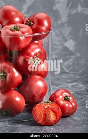 Grosses tomates fraîches sur fond gris. Tomates entières et tranchées en gros plan avec méta pour le texte. Art concept tomates dans le verre. Banque D'Images