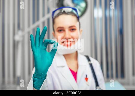 La femme médecin montre avec la main ok, vêtue d'EPI, dans le quartier. Copy Space, concept de la victoire de la maladie. Banque D'Images
