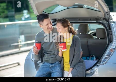 Homme et femme ayant un café près de sa voiture. Banque D'Images