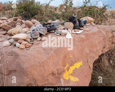 Vieilles chaussures déchirées laissées derrière avec des pierres sur un rocher avec une flèche jaune partiellement fanée quelque part en Espagne sur le chemin de St.James4 Banque D'Images