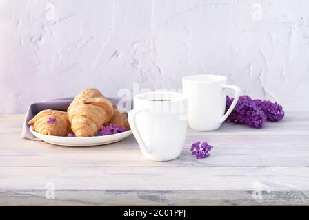 Deux belles tasses de café en porcelaine avec du lait et des croissants décorés de fleurs lilas sur une table en bois blanc. Concept de petit déjeuner parfait. Copie s Banque D'Images