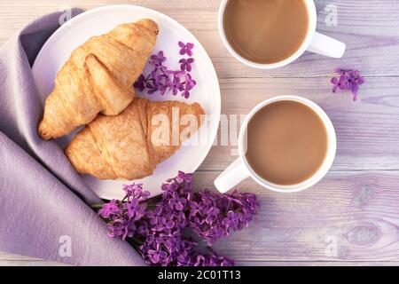 Deux belles tasses de café en porcelaine avec du lait et des croissants décorés de fleurs lilas sur une table en bois blanc. Concept de petit déjeuner parfait. Plat l Banque D'Images