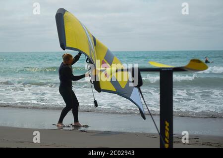 Un homme se tient sur une plage pratiquant avec une aile à main pour le surf d'aile hydrofoil. Banque D'Images