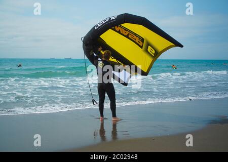 Un homme se tient sur une plage pratiquant avec une aile à main pour le surf d'aile hydrofoil. Banque D'Images