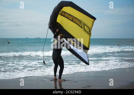 Un homme se tient sur une plage pratiquant avec une aile à main pour le surf d'aile hydrofoil. Banque D'Images