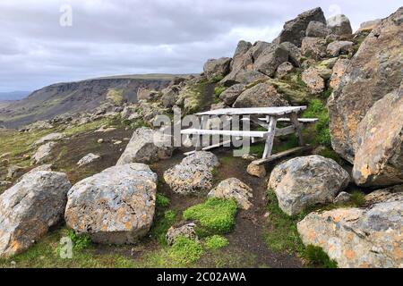 Une table de pique-nique en bois est installée sur les rochers surplombant les montagnes en arrière-plan avec des falaises rocheuses. Région de la cascade de Haifoss en Islande Banque D'Images