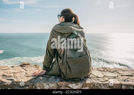 De tourisme de fille avec un sac à dos dans la solitude, s'assoit et regarde la mer Banque D'Images