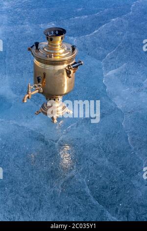 Un samovar rétro en cuivre se dresse sur la glace du lac avec un espace de copie. bouilloire russe au feu de bois. Magnifique glace bleue avec fissures. Verticale. Banque D'Images