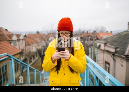 Jeune femme en imperméable jaune utilisant un smartphone Banque D'Images