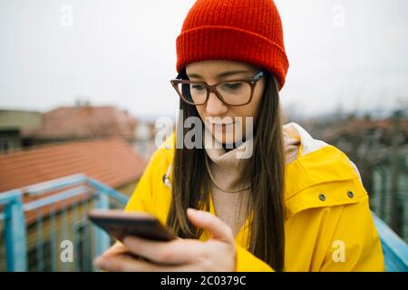 Jeune femme en imperméable jaune utilisant un smartphone Banque D'Images