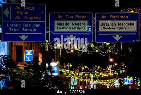 Panneau routier à Kuala Lumpur pendant les fêtes avec des lumières indiquant la place Merdeka et la Mosquée nationale de Malaisie Banque D'Images