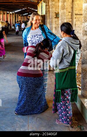 Un touriste essaie un long birman traditionnel (Sarong) aidé par deux femmes locales, le marché de Thaung Thut, le lac Inle, l'État Shan, Myanmar. Banque D'Images