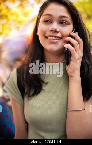 Belle jeune fille heureuse qui marche sur la rue du marché et qui parle sur un smartphone à l'heure du jour. Banque D'Images