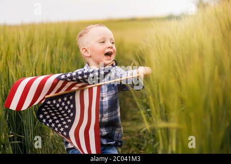 Un joli garçon blond est debout dans un champ avec un drapeau américain entre ses mains. Banque D'Images