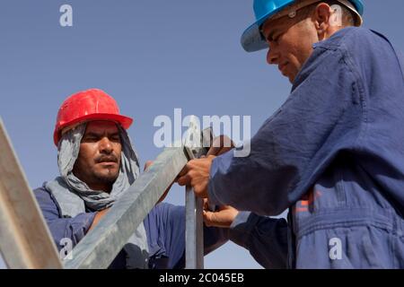 Les travailleurs assemblent des pylônes d'électricité pour transporter l'électricité à une nouvelle grande installation d'exploration pétrolière en cours de construction dans le désert du Sahara. Banque D'Images