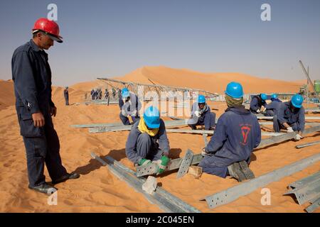 Les travailleurs assemblent des pylônes d'électricité pour transporter l'électricité à une nouvelle grande installation d'exploration pétrolière en cours de construction dans le désert du Sahara. Banque D'Images