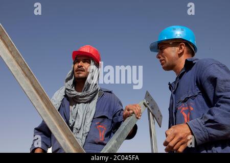 Les travailleurs assemblent des pylônes d'électricité pour transporter l'électricité à une nouvelle grande installation d'exploration pétrolière en cours de construction dans le désert du Sahara. Banque D'Images