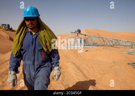 Les travailleurs assemblent des pylônes d'électricité pour transporter l'électricité à une nouvelle grande installation d'exploration pétrolière en cours de construction dans le désert du Sahara. Banque D'Images