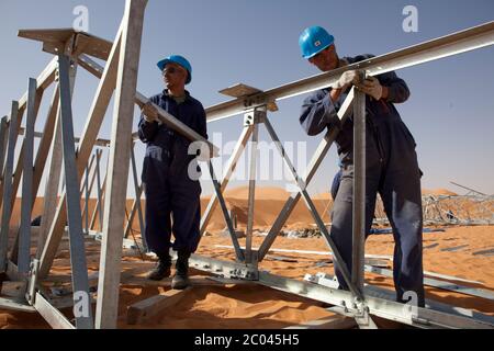 Les travailleurs assemblent des pylônes d'électricité pour transporter l'électricité à une nouvelle grande installation d'exploration pétrolière en cours de construction dans le désert du Sahara. Banque D'Images