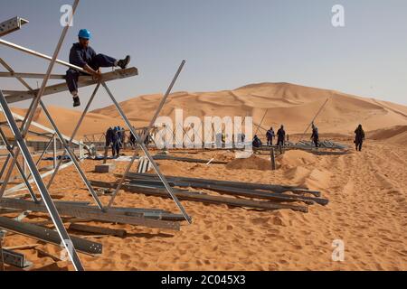 Les travailleurs assemblent des pylônes d'électricité pour transporter l'électricité à une nouvelle grande installation d'exploration pétrolière en cours de construction dans le désert du Sahara. Banque D'Images