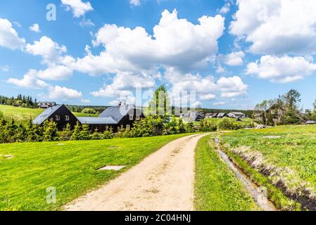 Journée d'été ensoleillée dans le village de montagne de Jizerka. Route de campagne poussiéreuse, prairies vertes et ciel bleu avec des nuages blancs, Jizera Mountains, République tchèque. Banque D'Images