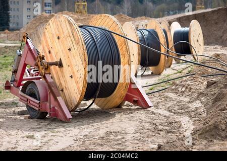 Concept de fourniture d'électricité pour les projets de construction. Plusieurs bobines en bois avec câble d'alimentation posé dans la tranchée. Banque D'Images