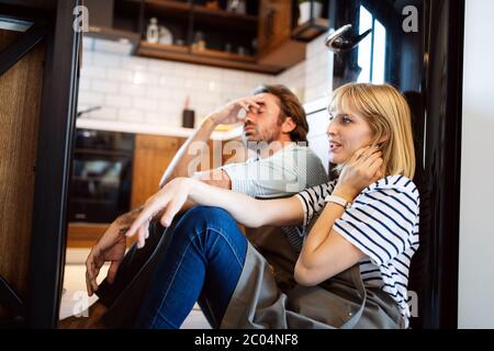 Les jeunes professionnels fatigué couple sitting on plancher de la cuisine après la cuisson Banque D'Images