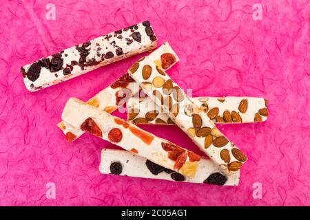Variété de blocs de tourron avec des noisettes, des amandes, des baies séchées et des fruits confits sur fond rose, vue en grand angle