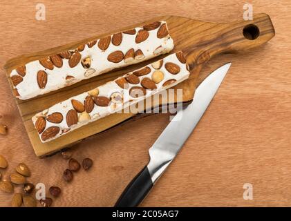 Blocs de turron doux aux amandes et noisettes sur planche à découper, avec couteau sur table en bois, vue en grand angle
