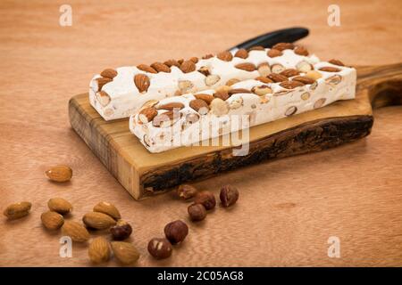 Blocs de turron doux aux amandes et noisettes sur planche à découper, avec couteau sur table en bois.