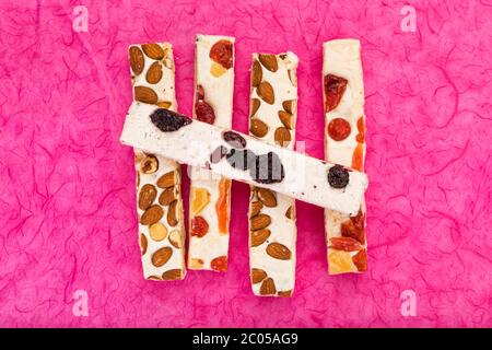 Variété de blocs de tourron avec des noisettes, des amandes, des baies séchées et des fruits confits sur fond rose, vue en grand angle
